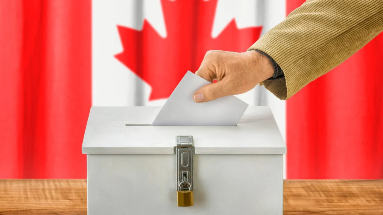 Man putting ballot in ballot box with Canadian flag in background.